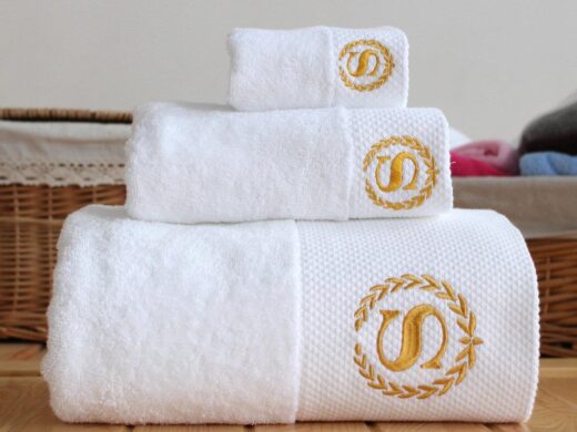 Stacked white linen towels with elegant gold 'S' monogram embroidery.