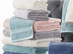 Plush, folded bath towels in soft colors stacked neatly on dark furniture.