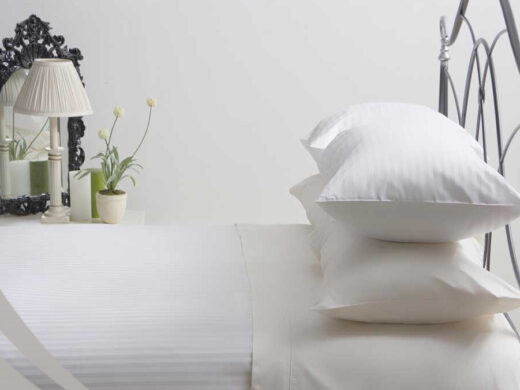 Close-up of luxurious **white linen** bedding, ornate mirror, and classic lamp.