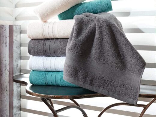 Neatly stacked luxury bath towels in cream, gray, white, and teal on a dark table.