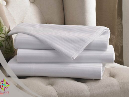 Stacked white satin-striped linen sheets on luxurious tufted beige upholstery.