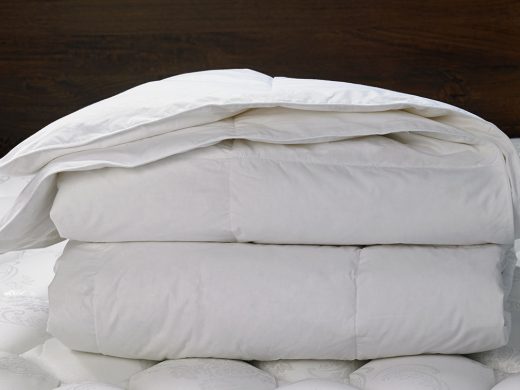 Fluffy white down comforters stacked on a bed with a dark wood headboard.