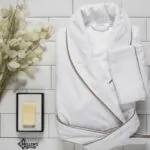 Luxury white terry cloth bathrobe with brown piping, spa setting.
