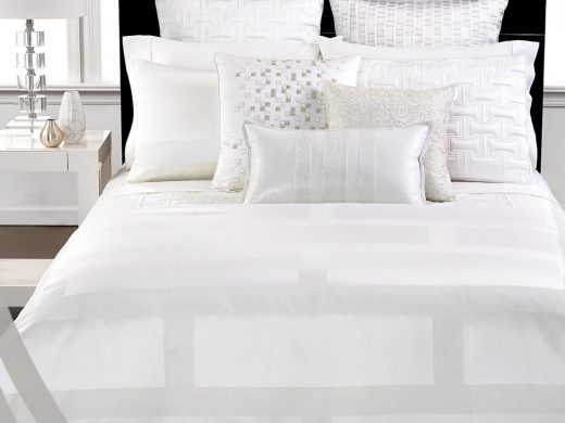 Luxurious white linen bedding with textured pillows, black headboard, crystal lamp.
