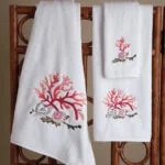 White bath towels with red coral and seashell embroidery on a dark rack.