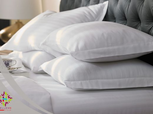 Luxurious stack of crisp white pillows on high-end bedding with a dark headboard.