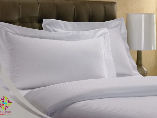 Crisp white hotel linen, stacked pillows, and dark brown leather headboard detail.