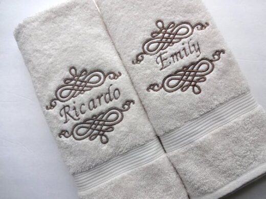 Personalized white bath towels embroidered with brown names 'Ricardo' and 'Emily'.