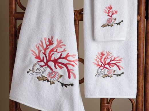 Embroidered white coral bath towels on a dark rattan rack.