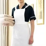 Smiling hotel housekeeping attendant in uniform holding folded towels.